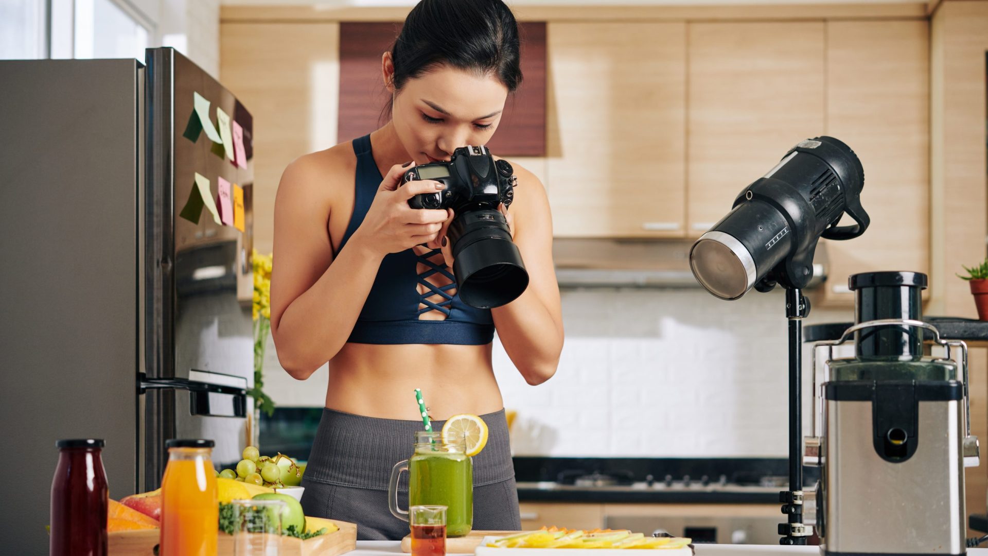 Food blogger setting professional light equipment when taking photos of green smoothie ingredients on her kitchen counter