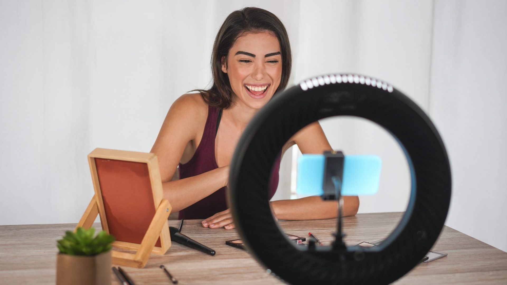 Young influencer woman creating social media videos with smartphone camera while putting on make up - New digital jobs trends, technology, cosmetics and fashion concept - Focus on her face